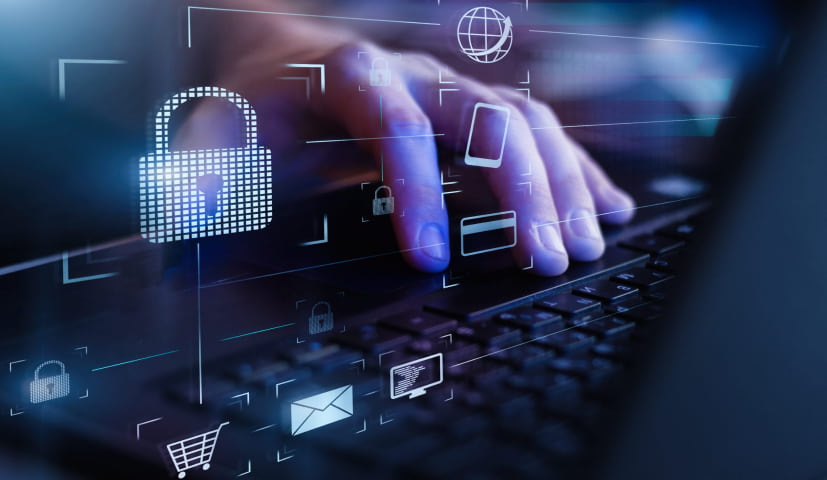 A hand typing on a keyboard with cyber security logos floating on the screen.
